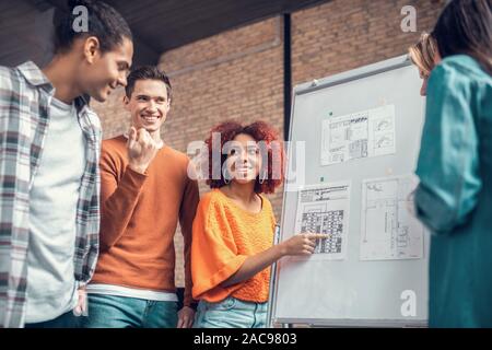 Speaking with friends. Dark-haired student smiling while speaking with friends about group project Stock Photo