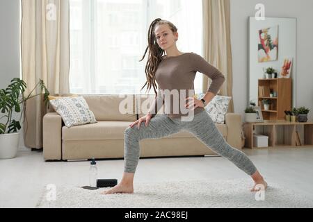 Young barefoot woman in leggins and pullover stretching legs during exercise Stock Photo