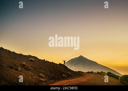Concept of succes and freedom with happiness - standing man with up arms enjoying the view of a mountain volcano in background - trekking and adventur Stock Photo