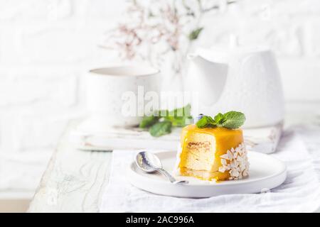 Piece of mango mousse cake on plate over white wooden table. Stock Photo