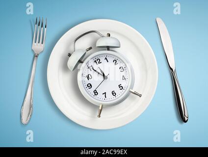 Concept of intermittent fasting, lunchtime, diet and weight loss. Clock on plate. Stock Photo