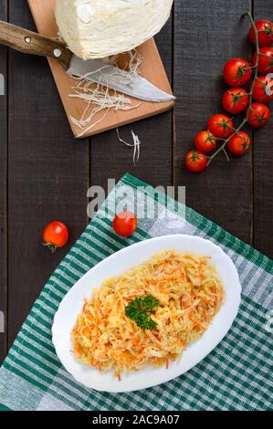 Garnish of stewed cabbage on a white plate on a rustic wooden background. Top view. Stock Photo