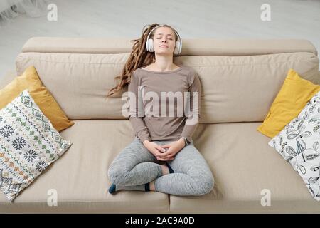 Restful woman in activewear sitting on couch and listening to peaceful music Stock Photo
