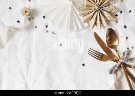 Christmas, New Year composition. Decorative table setting. Paper stars, golden cutlery and confetti stars on white linen background. Celebration Stock Photo