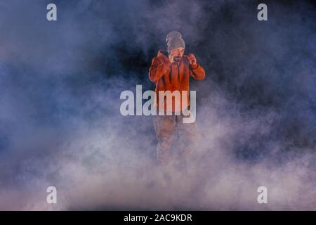 Male breakdancer jumps off high in the air while performing a cool dance move, a lot of smoke in the background. Stock Photo