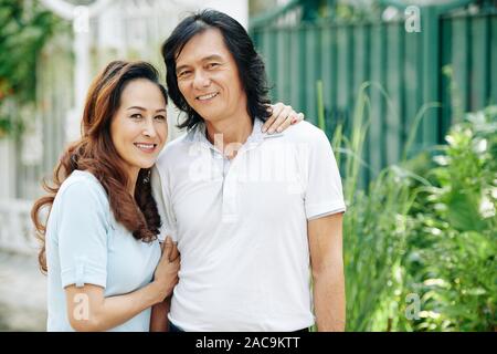 Positive Asian middle-aged couple hugging and posing in the street together Stock Photo