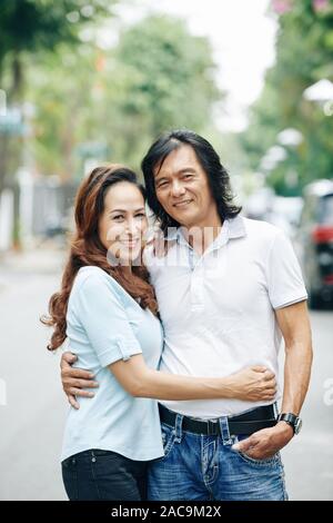 Happy mature couple in love hugging in the street and looking at camera Stock Photo