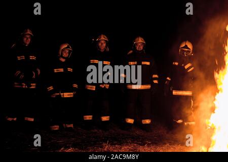 Group of firemen in protective suits putting out a fire Stock Photo