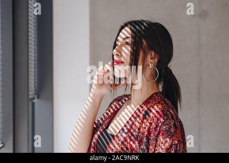Portrait of  confident businesswoman standing in new office and talking over phone with partners negotiating a new deal. Creative portrait using light Stock Photo