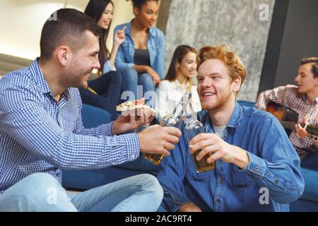 Young men and women having fun together indoors two guys sitting close-up drinking beer cheers eating pizza joyful Stock Photo