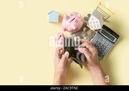Man hand open an empty wallet with piggy bank and model house on yellow background, saving money concept Stock Photo