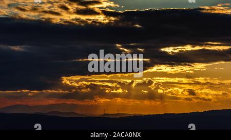 Dramatic sunset in the black forest with light strokes and silhouettes of some wind power generators Stock Photo