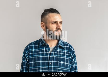 Confident and concentrated mature bearded man wearing in trendy checkered shirt, standing isolated on grey background with copy space, looking away Stock Photo