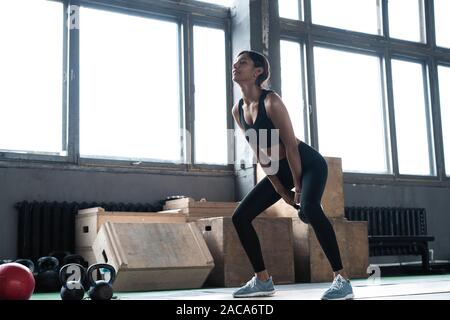 Side view of young beautiful woman with perfect body in sportswear working out with kettle bell at gym. Stock Photo