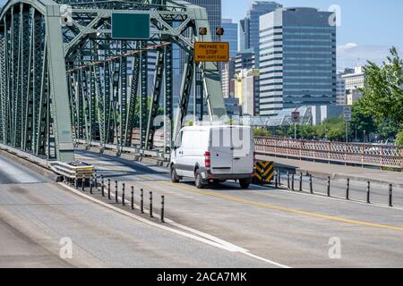 Comfortable compact white commercial cargo mini van for local deliveries and carry small business driving on the road on green metal truss bridge Stock Photo