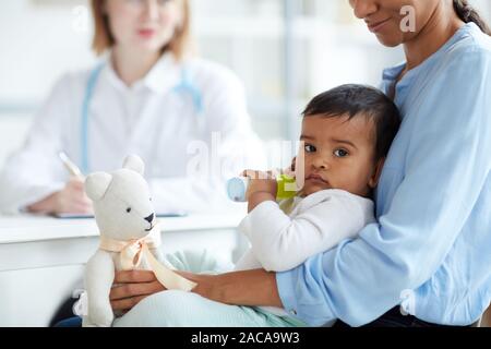 Portrait of baby boy lying on mother's knees and looking at camera while they visiting doctor at hospital Stock Photo