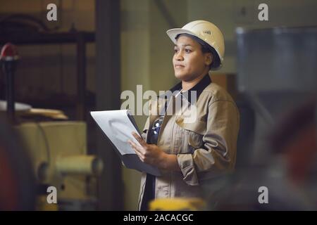 Waist up portrait of female foreman holding clipboard while supervising production at factory, copy space Stock Photo