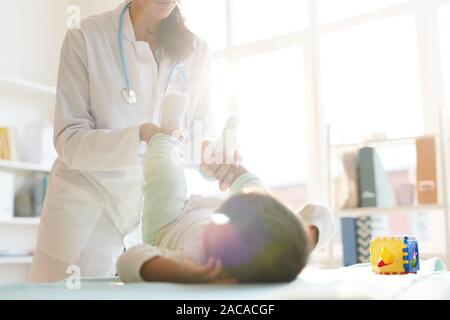 Female doctor in white coat standing and examining the baby while he lying on the table at hospital Stock Photo