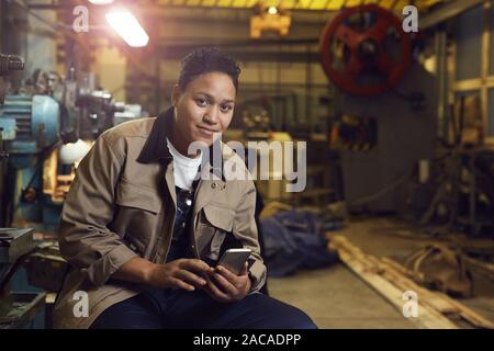 Portrait of contemporary mixed-race woman smiling at camera while posing in factory workshop, copy space Stock Photo