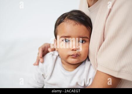 Portrait of African baby boy looking at camera while sitting on his mother's knees Stock Photo