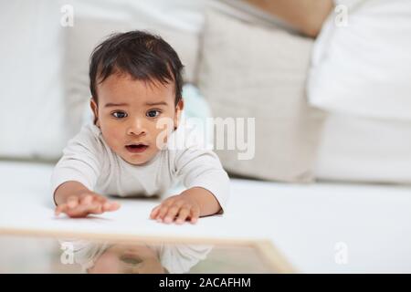 Cute baby girl with dark hair lying and playing on the floor Stock Photo