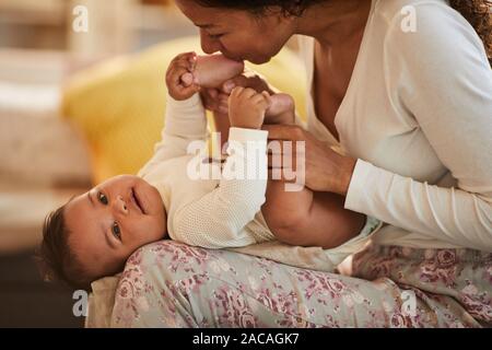 Portrait of caring African-American mother kissing feet of cute baby boy while cuddling, copy space Stock Photo