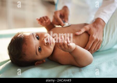 African newborn lying on back while doctor listening to his heartbeat with stethoscope at hospital Stock Photo