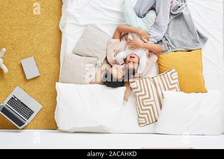High angle view of happy young mother lying and embracing her child in the bed in the bedroom at home Stock Photo