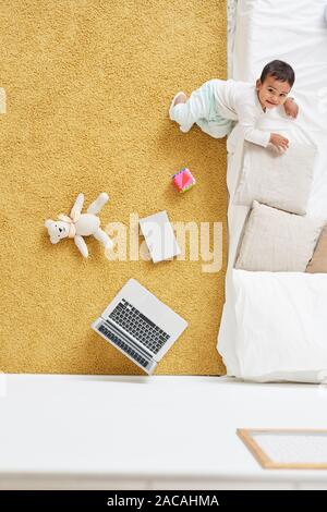High angle view of cute toddler smiling at camera while playing on the floor with toys Stock Photo
