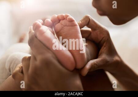 Close up portrait of African-American woman holding tiny feet of cute baby in sunlight, copy space Stock Photo