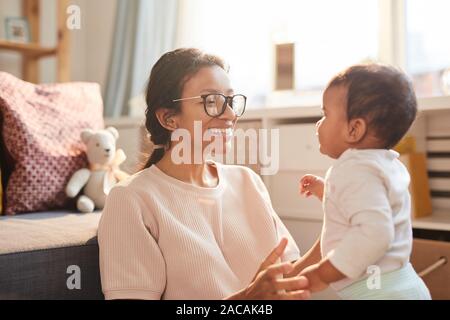 Happy young mother in eyeglasses talking to her little child in the room at home Stock Photo