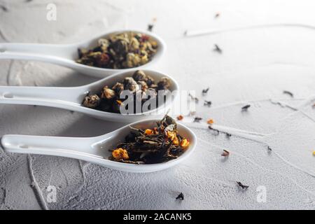Different varieties of tea leaves in white measuring spoons on a white textured background. To brew tea, a delicious and healthy beverage, Chinese tea Stock Photo