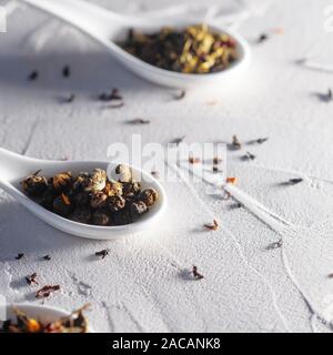 Different varieties of tea leaves in white measuring spoons on a white textured background. Three spoons with different teas, Oolong, green and fruity. Stock Photo