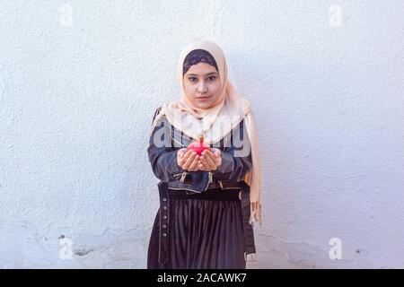 Beautiful middle-eastern girl holding pomegranate fruit. Cute Arabian Muslim woman received unique present - exotic fruit pomegranate Stock Photo