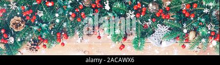 Christmas border with fir branches, red holly berries, cones and snowflakes on wooden background Stock Photo