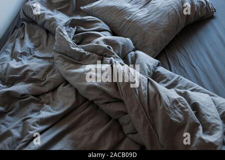 A gray cotton sheet and blankets with pillows on the bed Stock Photo