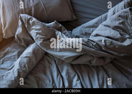 Top view crumpled bed in the morning after sleep. Gray cotton sheet and blankets on the bed Stock Photo