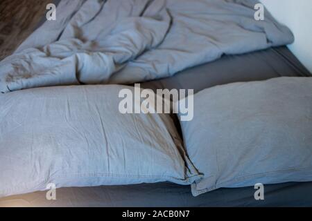 Closeup of gray pillows and blankets with a sheet on the bed Stock Photo