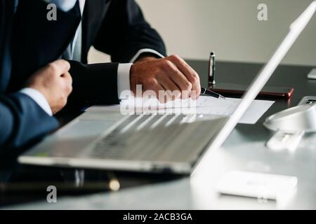Detail of the hands of some men working in the office with pen and laptop paper Stock Photo