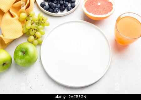 Fresh organic fruits, fruit juice and empty white plate with copy space for text. Vegan vegetarian food concept, healthy eating, dieting Stock Photo