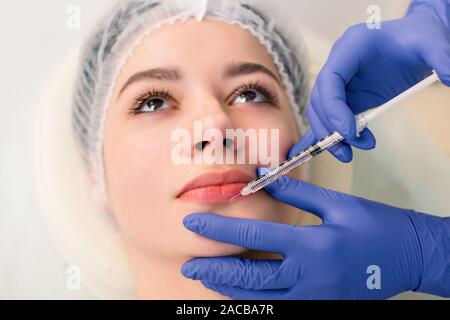 A beautiful woman receives a filler injection on the lips. Young woman receiving a botox injection in her lips, close up Stock Photo