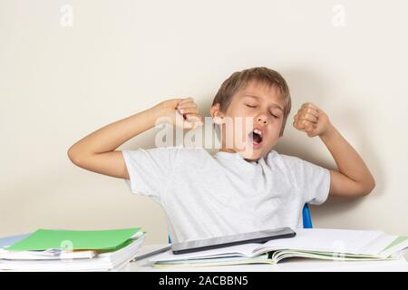 Tired kid yawning when making homework with books, notebooks and digital tablet Stock Photo