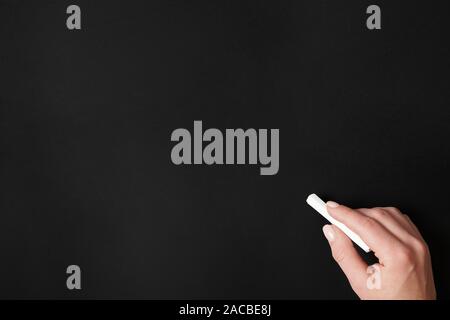 hand holding chalk against blank chalkboard background Stock Photo