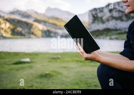 A beautiful caucasian blonde woman reads a book in a mountainous landscape with a lake Stock Photo