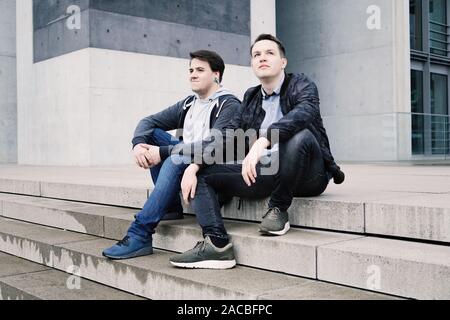 two male teenage friends or brothers two male teenage friends sitting on concrete steps or staircase outside - urban youth lifestyle Stock Photo