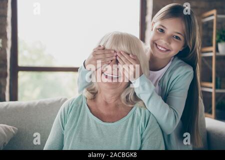 Guess who. Photo of two adorable people cute aged granny little granddaughter surprise visit sit cozy sofa grandchild closing grandma eyes house Stock Photo