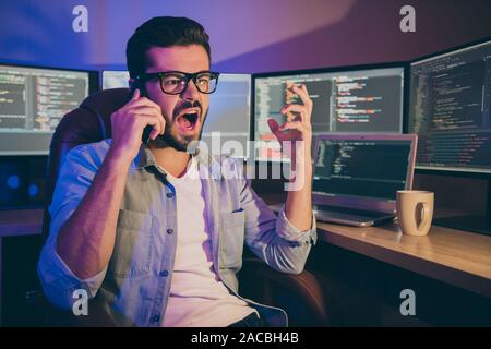 Photo of it specialist overworked guy night sitting chair website debugging problems service error speaking telephone tired exhausted yelling crazy Stock Photo