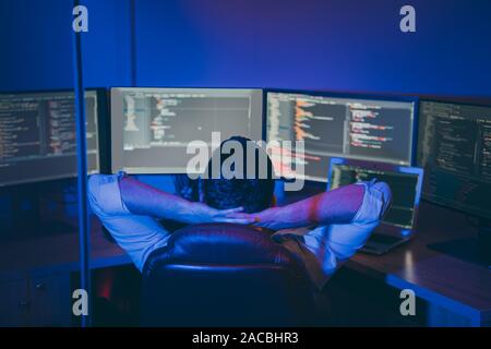 Rear behind view photo of it skilled specialist guy sitting comfy office chair holding hands behind head looking many monitors testing team finishing Stock Photo