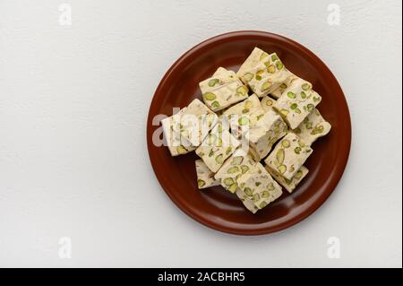 Eastern Arabic nougat sweetness with pistachios on a brown ceramic plate on a light background. Top view Stock Photo