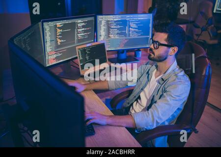 Photo of it specialist guy sitting comfy office chair holding hands on keyboard looking many monitors testing website debugging developer expert dark Stock Photo